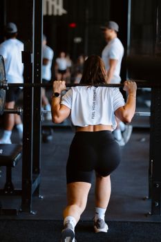 A woman performs a barbell squat in a gym with natural lighting, reflecting strength and fitness.
