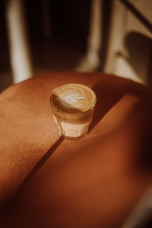 Free A serene image of a latte served in a glass, placed on a cozy café chair with warm sunlight streaming in. Stock Photo