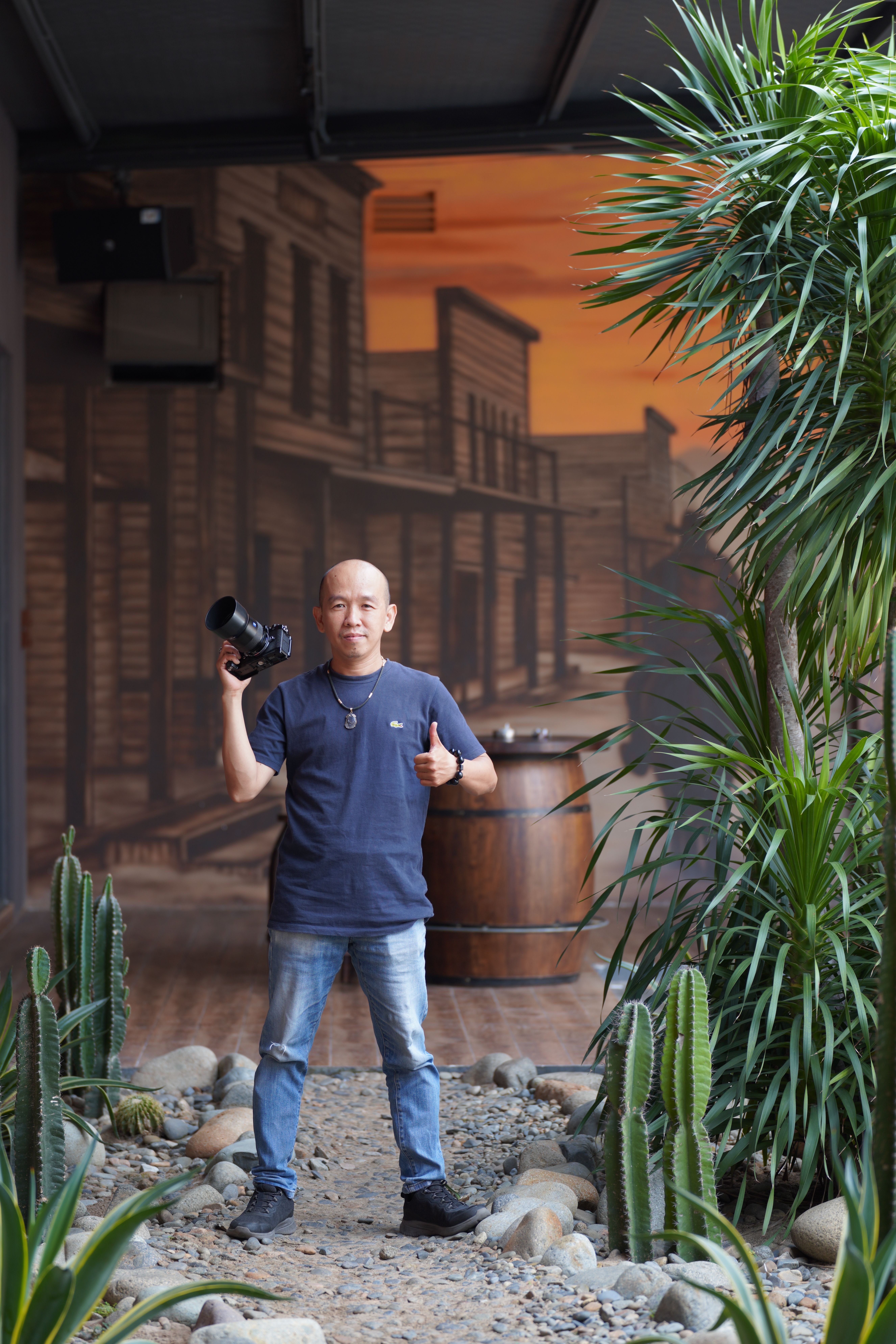 Photographer posing with camera in a western-style interior setup with cactus plants.