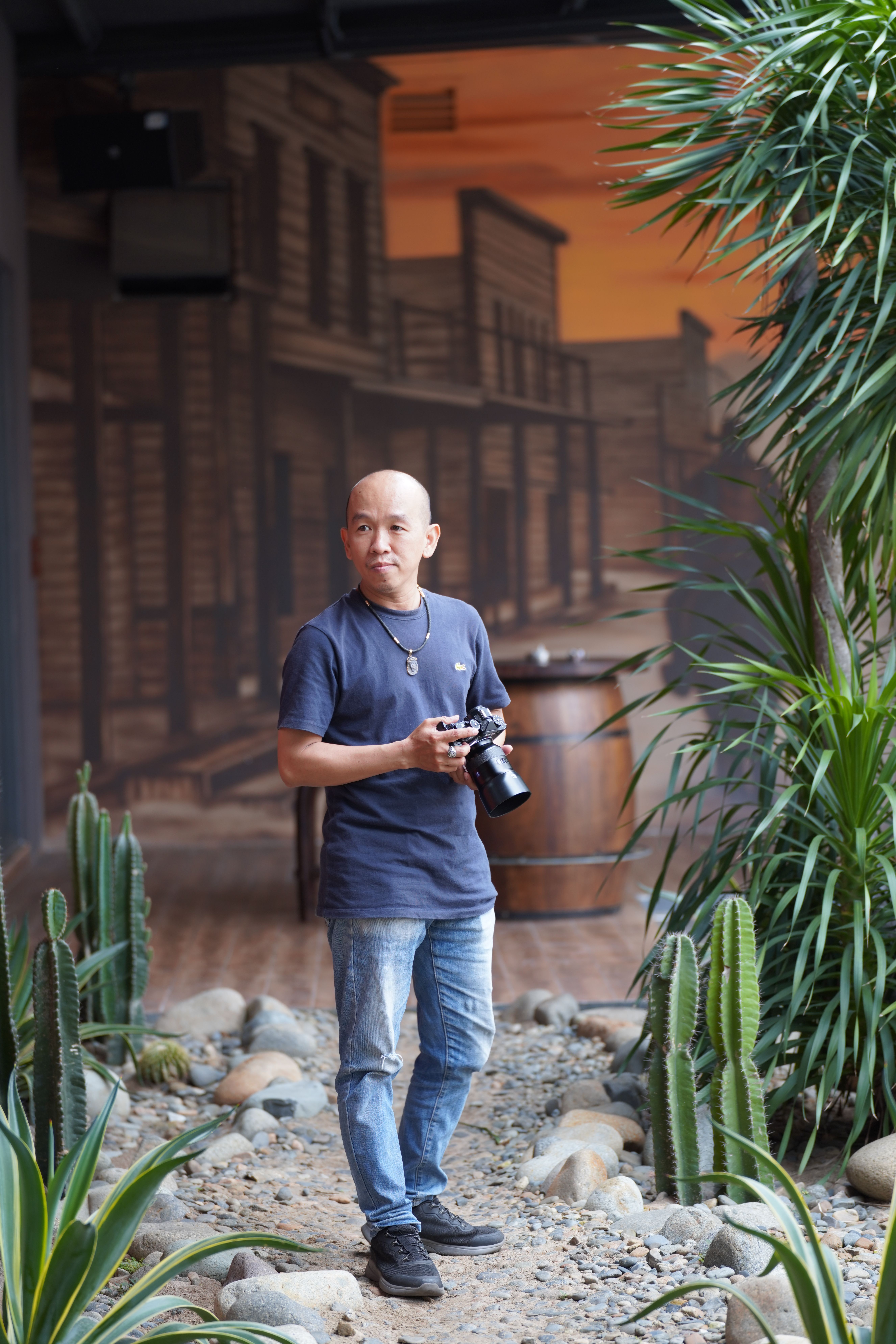 Man holding camera in an urban desert-themed setting with plants.