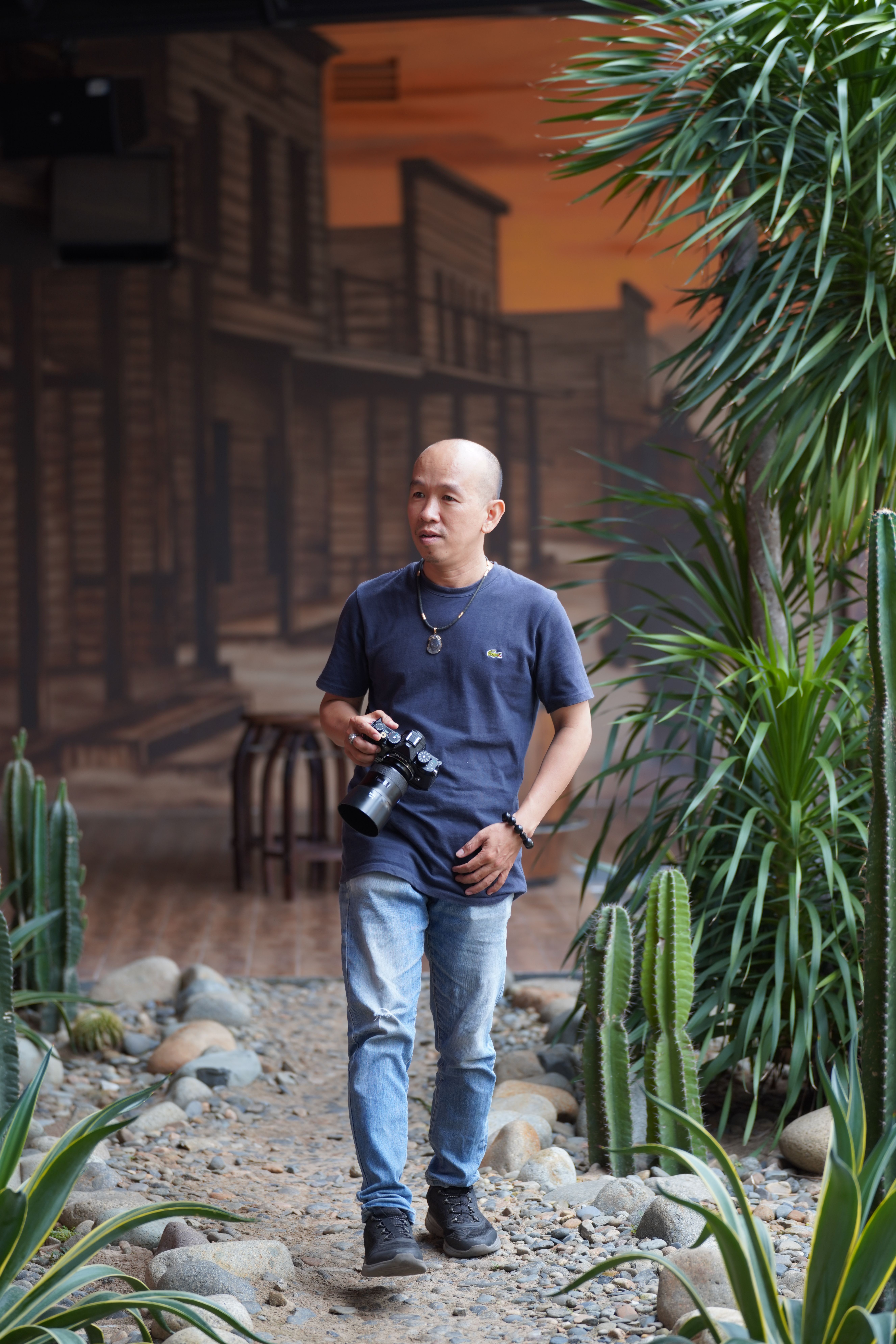 A man carrying a camera walks through a tropical-themed indoor area with plants and decor.