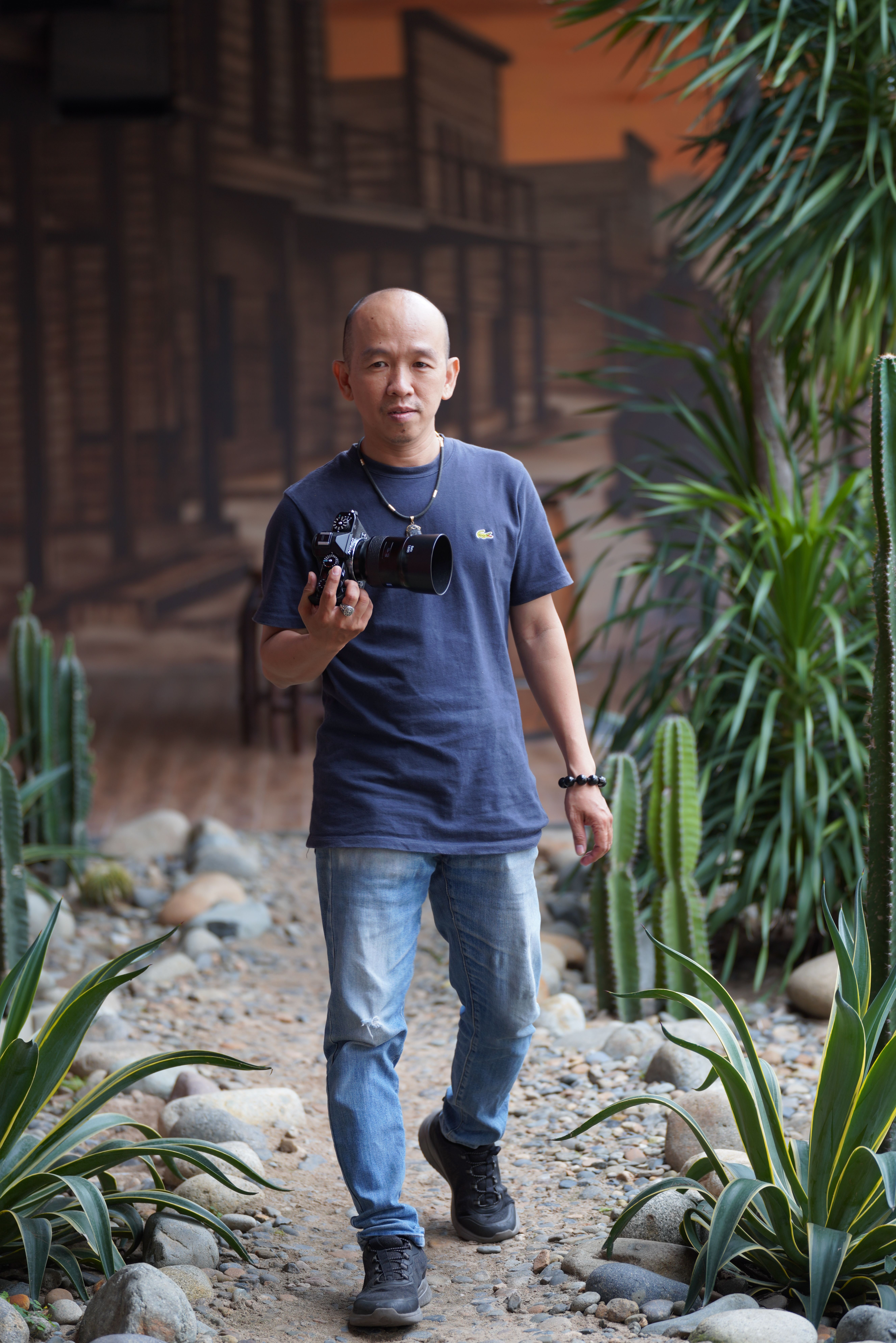 Casual photographer holding camera walking through a desert-themed indoor setting with greenery.