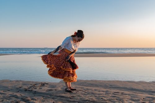 Free A woman in traditional folk attire gracefully dances on a serene beach during sunset. Stock Photo