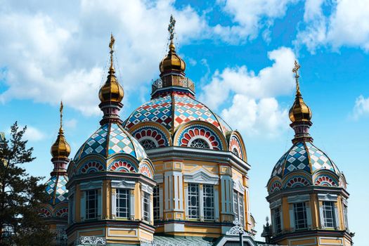 Colorful domes of the Ascension Cathedral in Almaty against a blue sky.