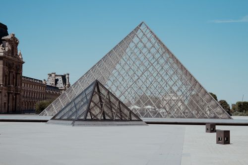 Free The glass pyramid at the Louvre Museum in Paris stands majestically under a clear blue sky. Stock Photo