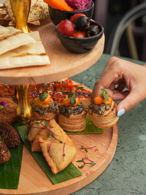 Free Hand selecting a gourmet pastry from a tiered platter with varied appetizers. Stock Photo