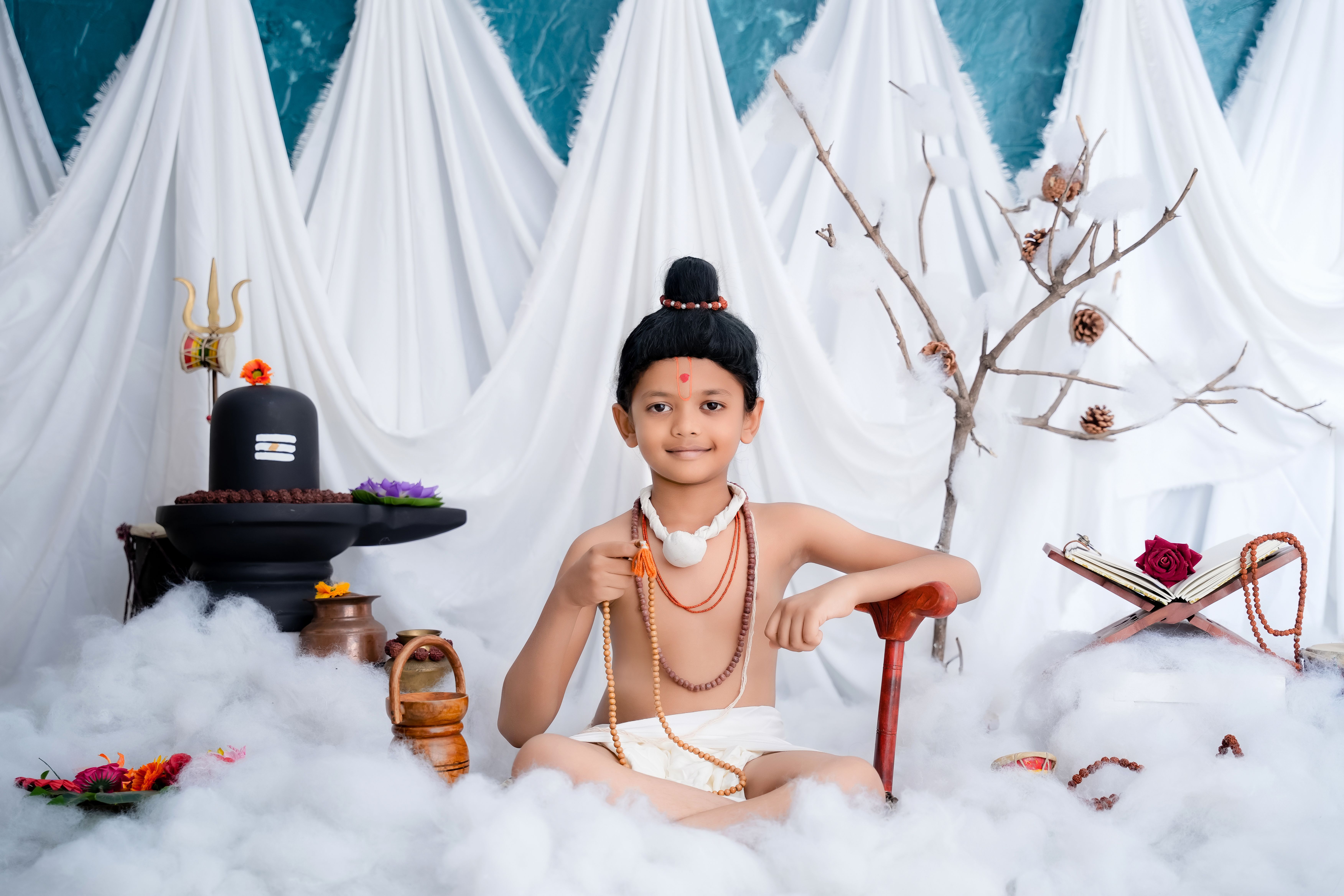 A child dressed in traditional Hindu attire with religious items, sitting calmly indoors.