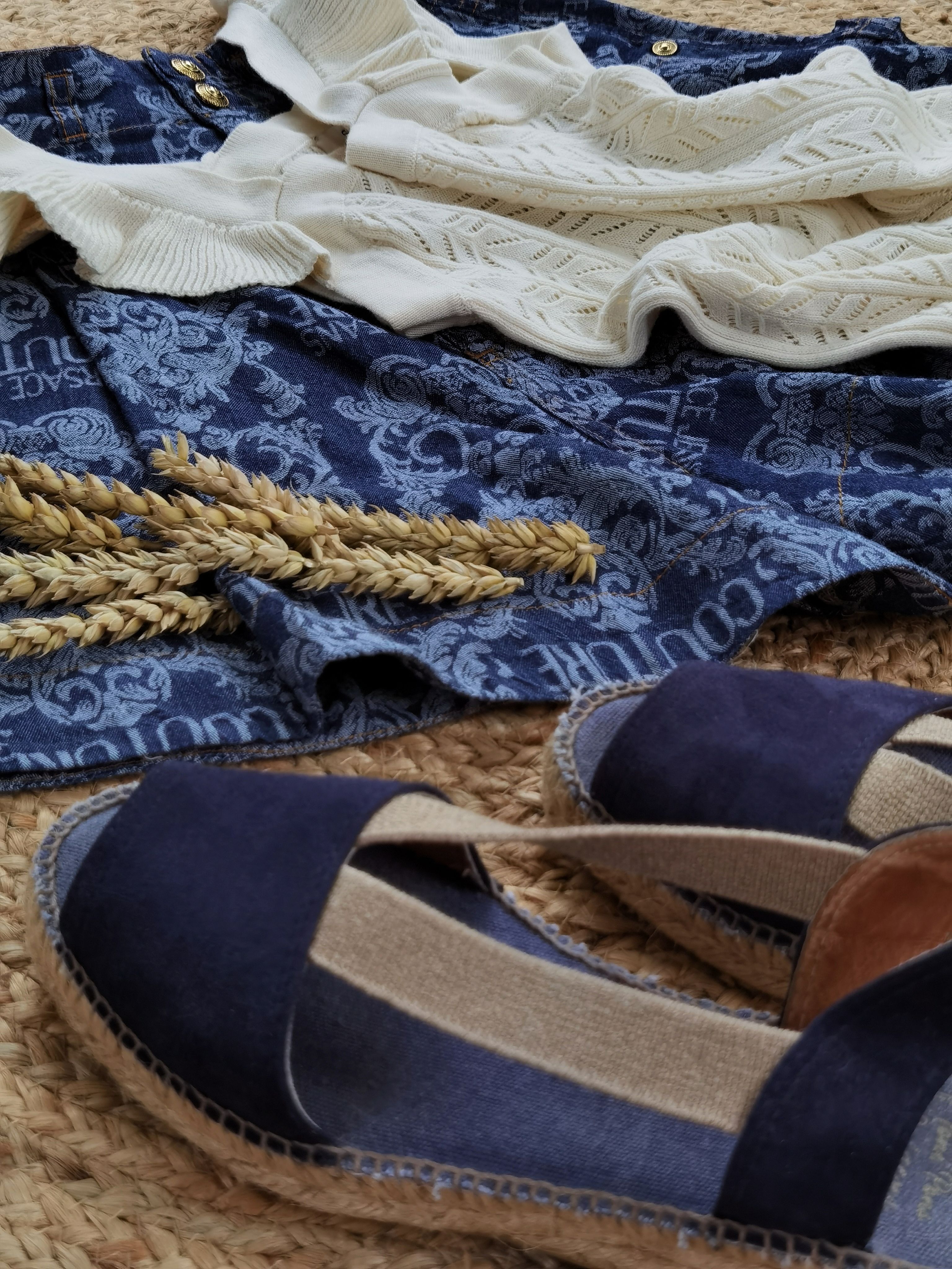 Stylish summer flat lay featuring blue sandals, patterned dress, and wheat accents.