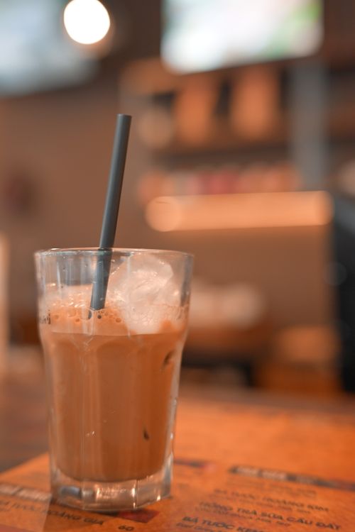 Free Close-up of an iced coffee in a glass, placed on a cafe table with a straw. Stock Photo