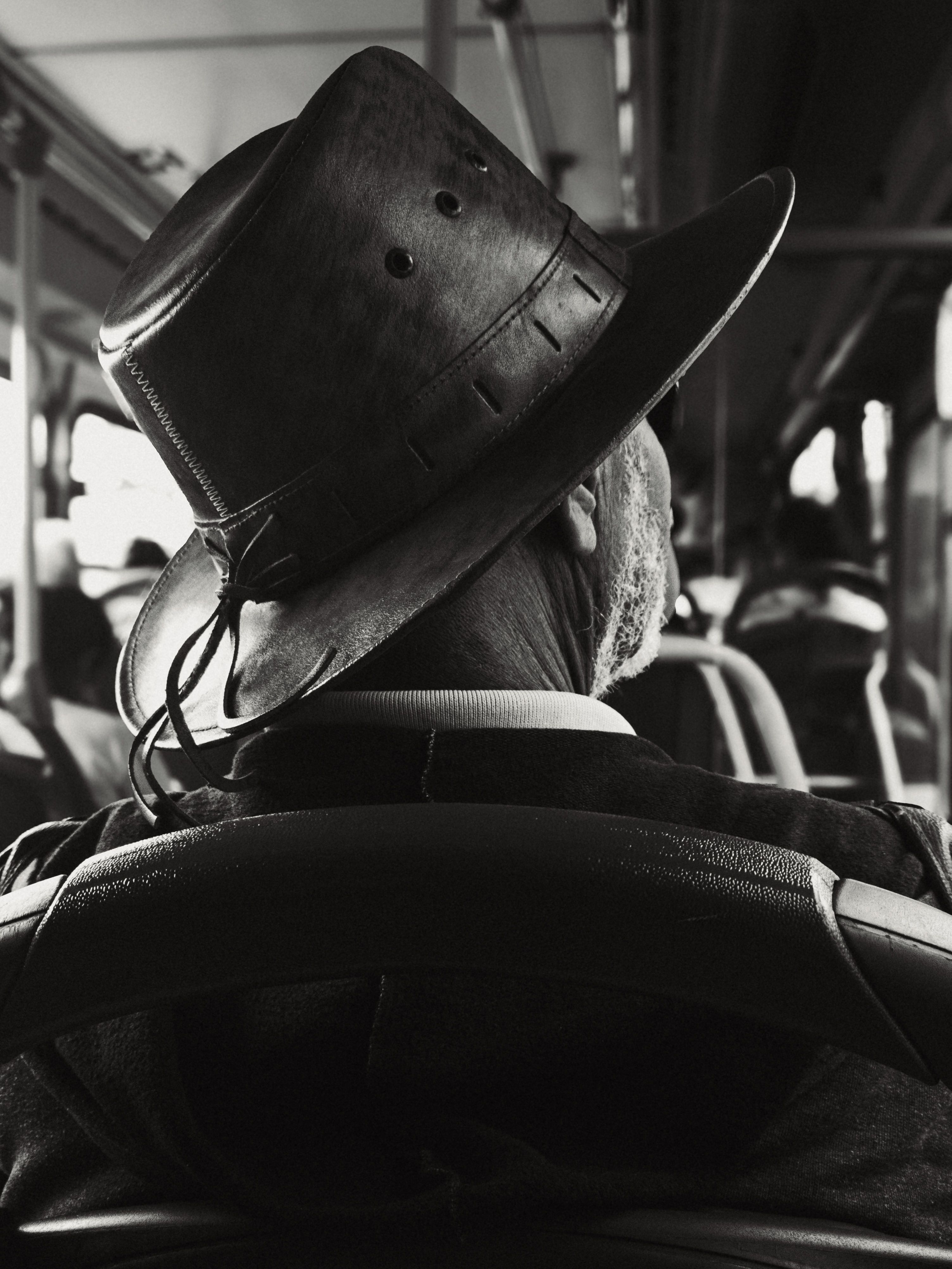 Black and white photo of a senior man wearing a hat on a bus, evoking nostalgia.