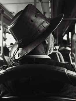 Black and white photo of a senior man wearing a hat on a bus, evoking nostalgia.