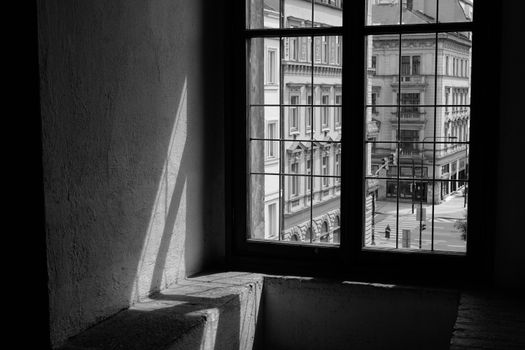 A monochrome view of Prague's architecture seen through a window, with dramatic shadows and historic buildings.