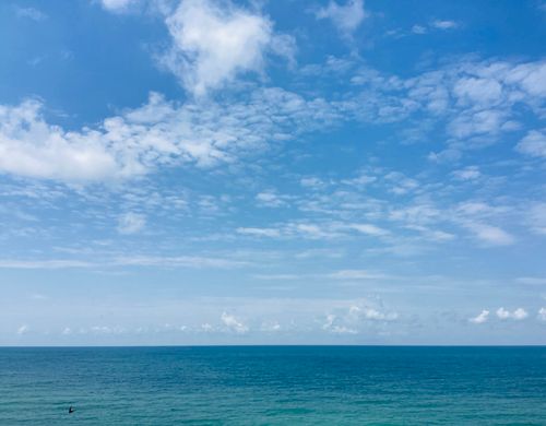 Free A peaceful seascape featuring a tranquil ocean under a bright blue sky with fluffy clouds. Stock Photo