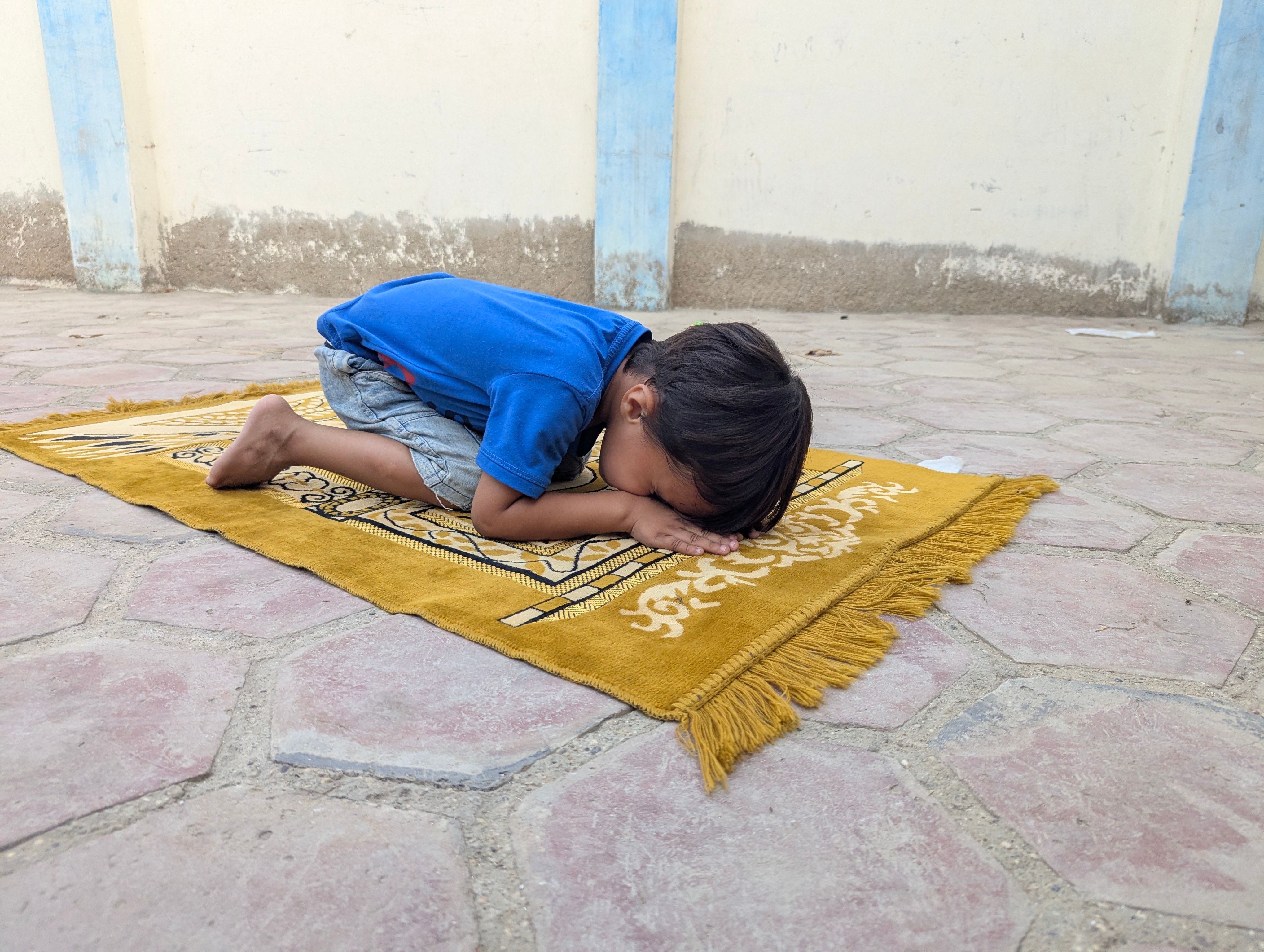 Child kneeling on a prayer mat outdoors, symbolizing innocence and spirituality