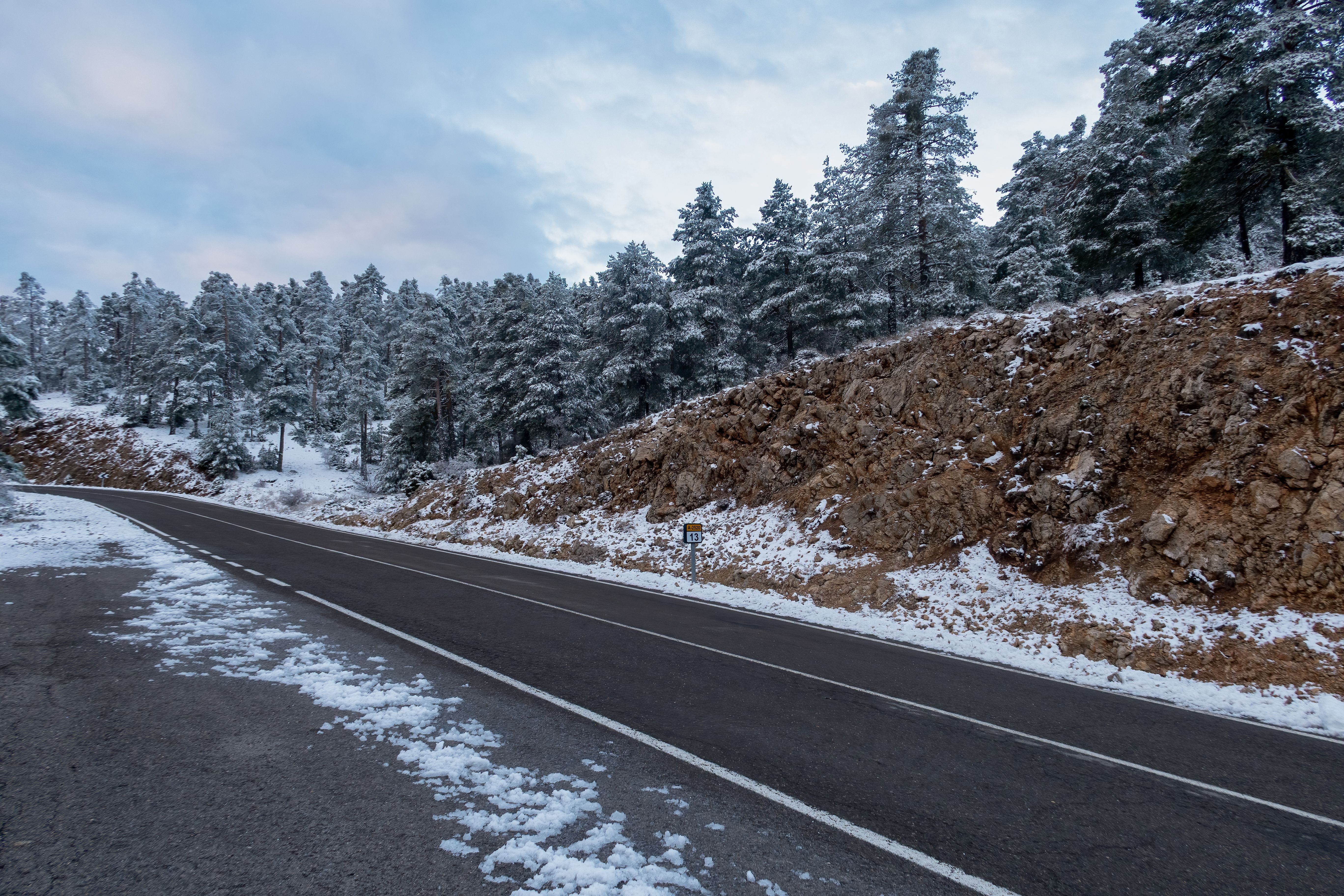 A snow-lined road climbing through pine forest