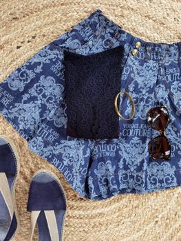 Stylish denim shorts with lace top, jewelry, sunglasses, and shoes on woven mat.