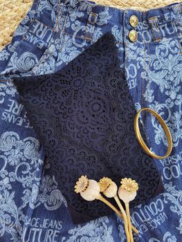 Elegant lace fabric on patterned denim with a gold bangle and decorative dried flowers.