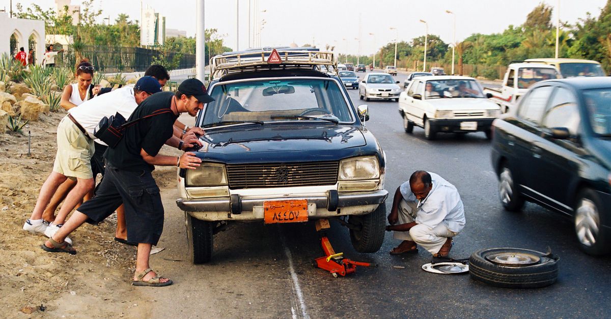 A group assists in repairing a car on a busy roadside, emphasizing teamwork and roadside assistance.