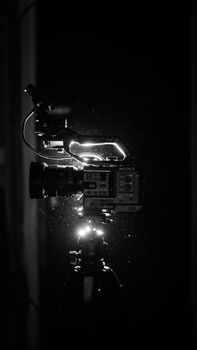 Black and white photo of a professional video camera illuminated with studio lights, capturing dust particles.