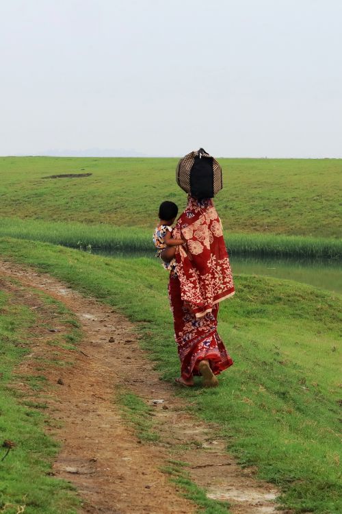 Free A woman in vibrant traditional attire walks with her child through lush greenery, embodying cultural heritage. Stock Photo