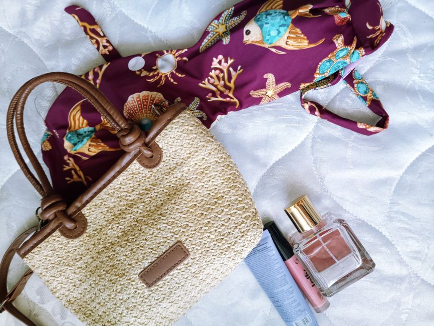 Flat lay of summer essentials with straw bag, swimwear, and cosmetics on a light background.