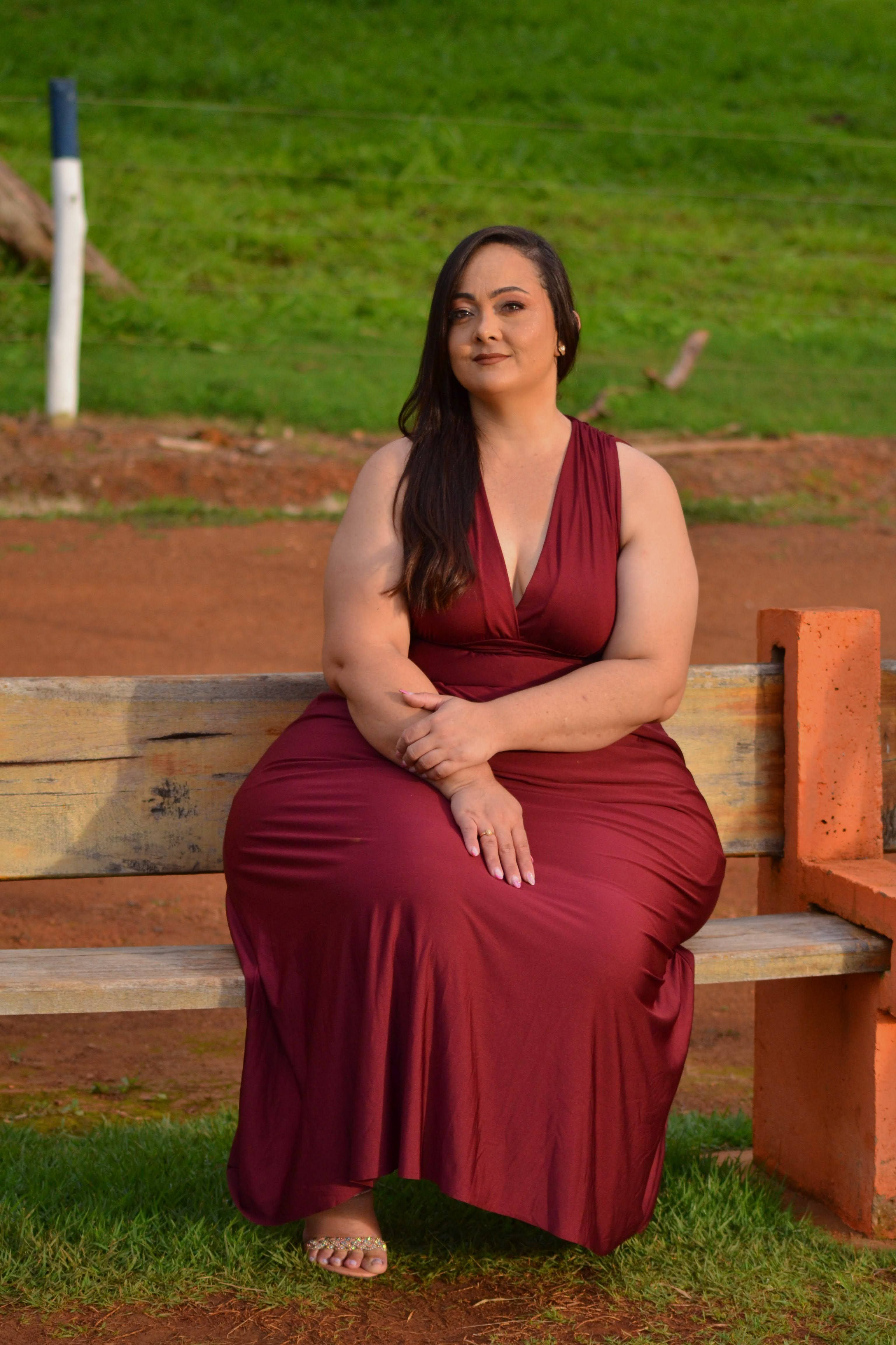 Confident woman in red dress sitting on a park bench, outdoors.