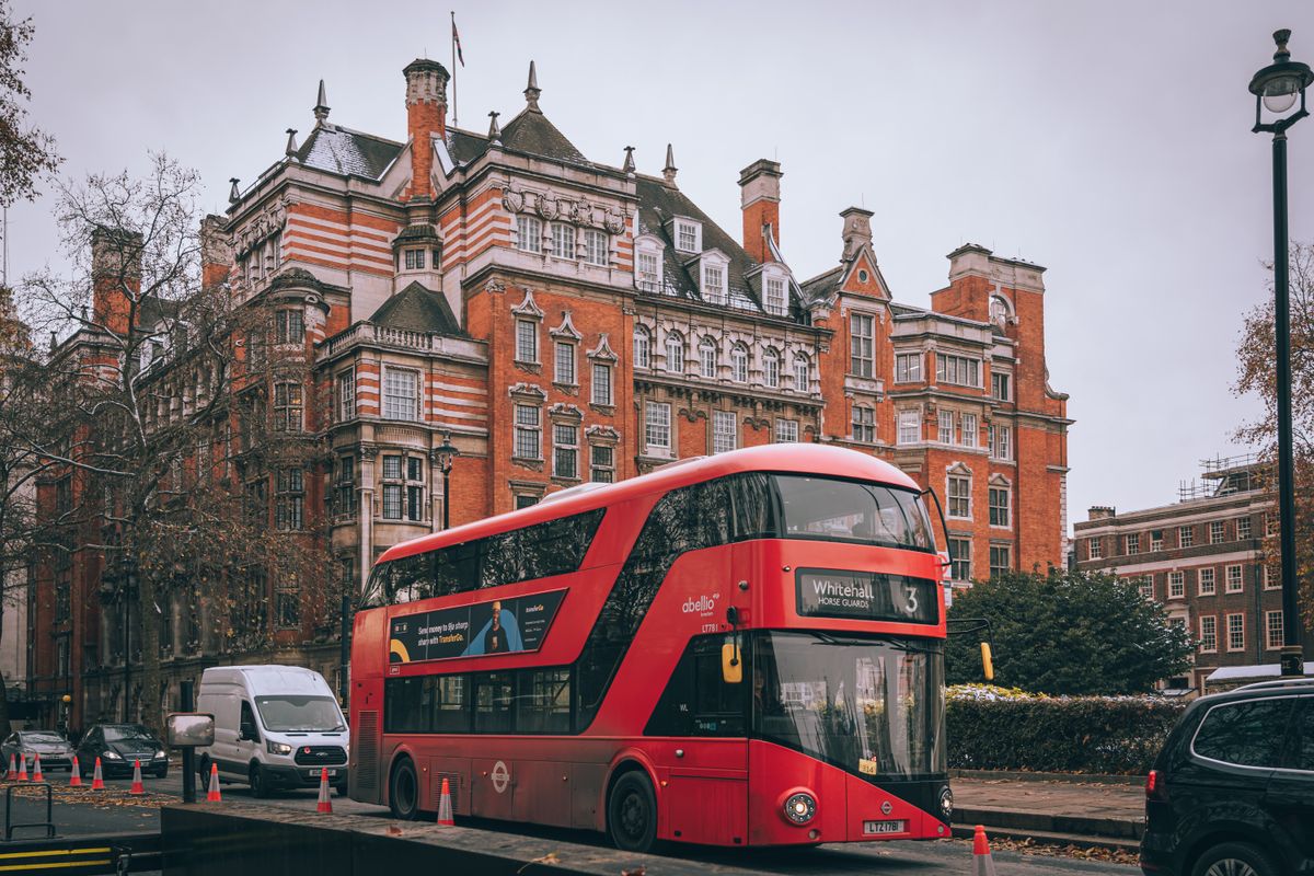 Autobuz roșu etajat pe o stradă din Londra, mărginită de clădiri clasice