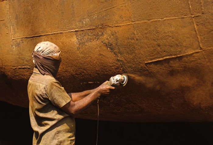 Worker grinding rust from a steel surface before coating