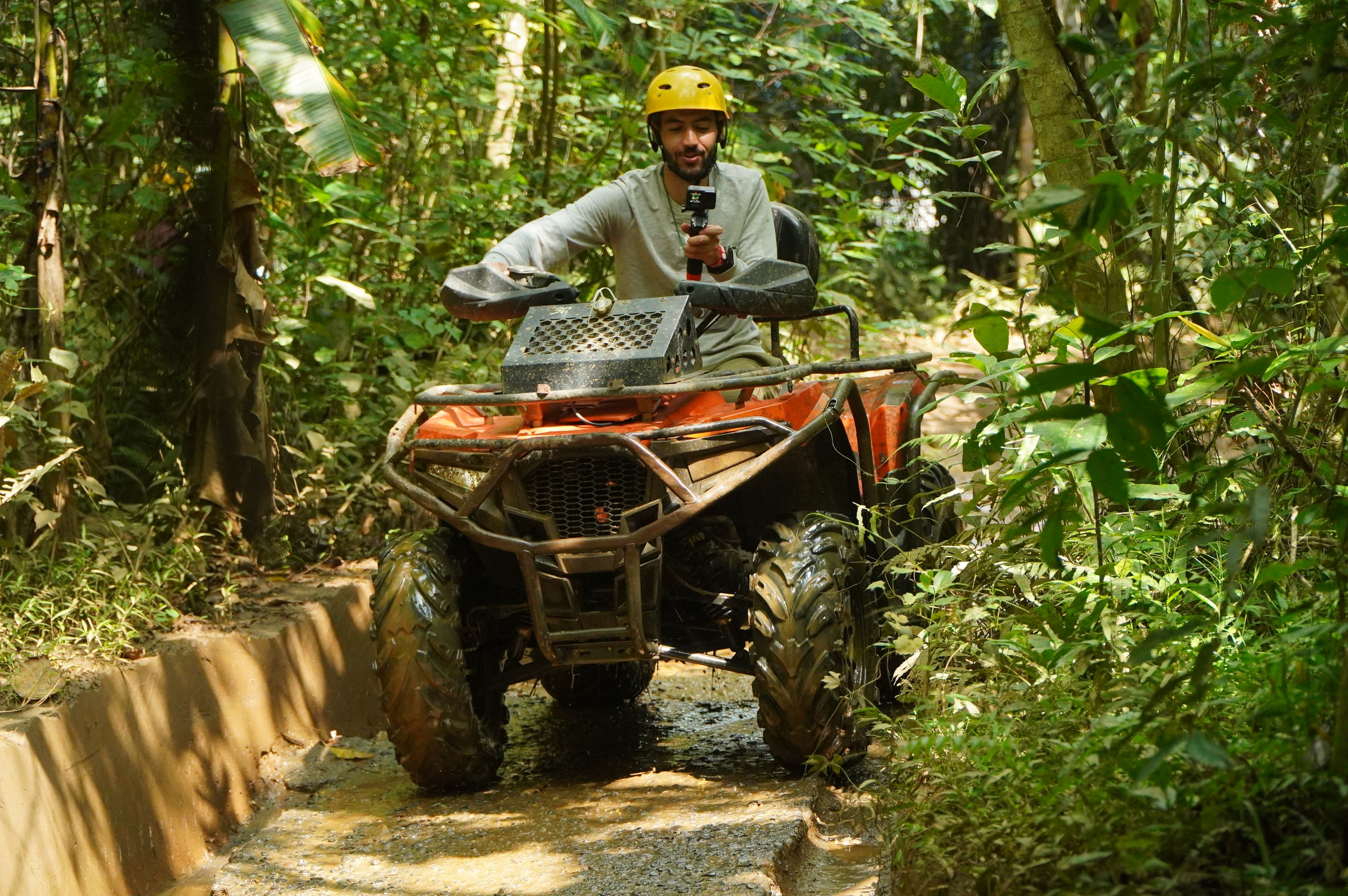 A man on an ATV navigates a jungle trail wearing safety gear, experiencing an outdoor adventure.