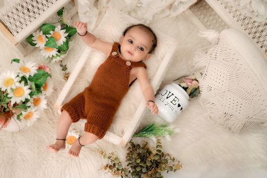 Cute baby in brown romper lying on a fluffy bed surrounded by flowers.