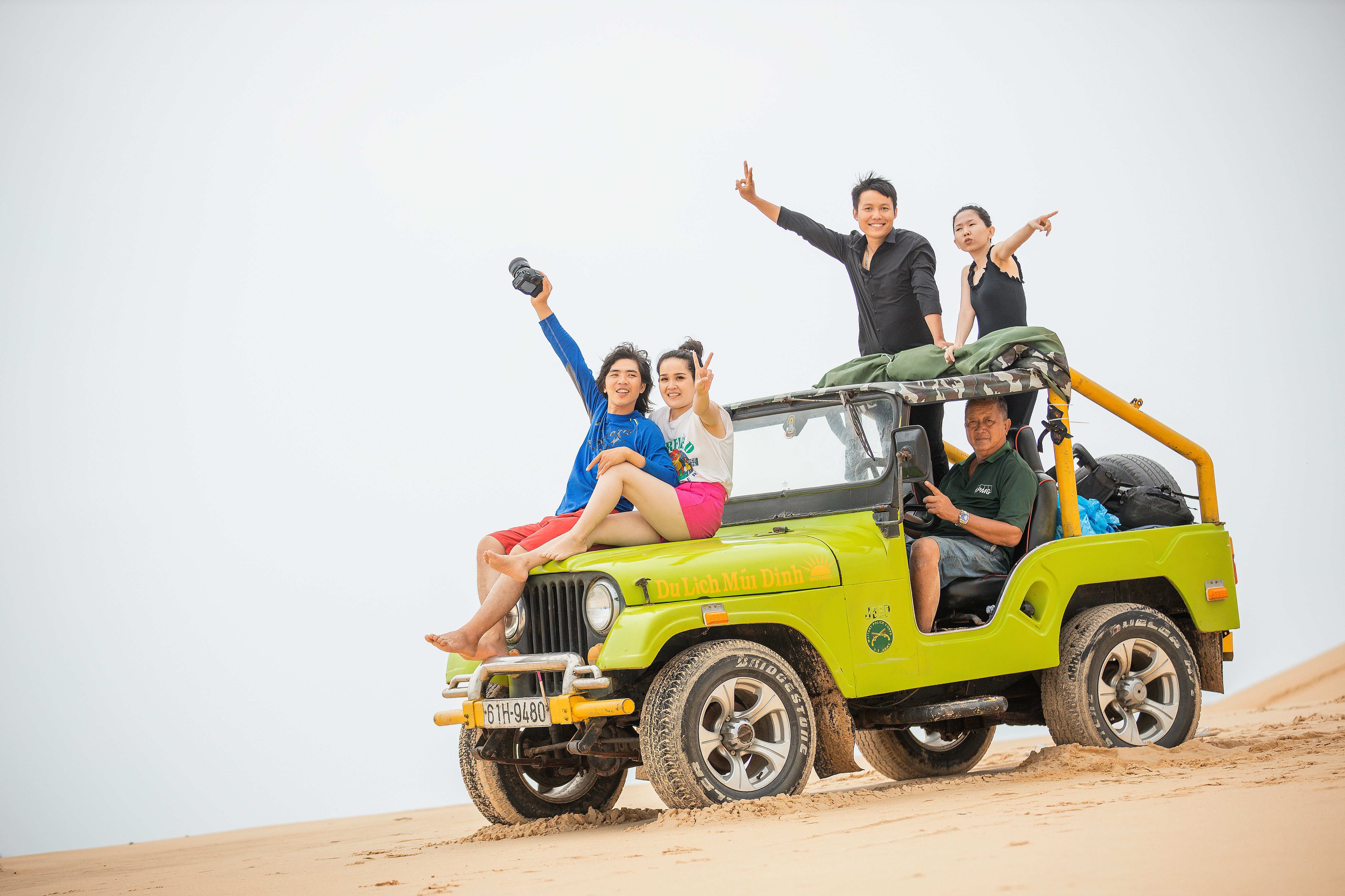 Friends enjoying an off-road adventure in a lime green jeep on sand dunes, exuding joy and exploration.
