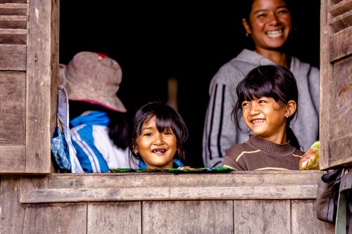 Free Two young girls smiling through a rustic wooden window, showcasing joy and human connection. Stock Photo