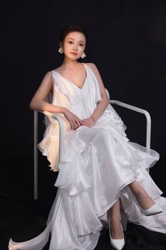 Elegant portrait of a woman in a flowing white silk gown sitting on a chair, exuding sophistication.