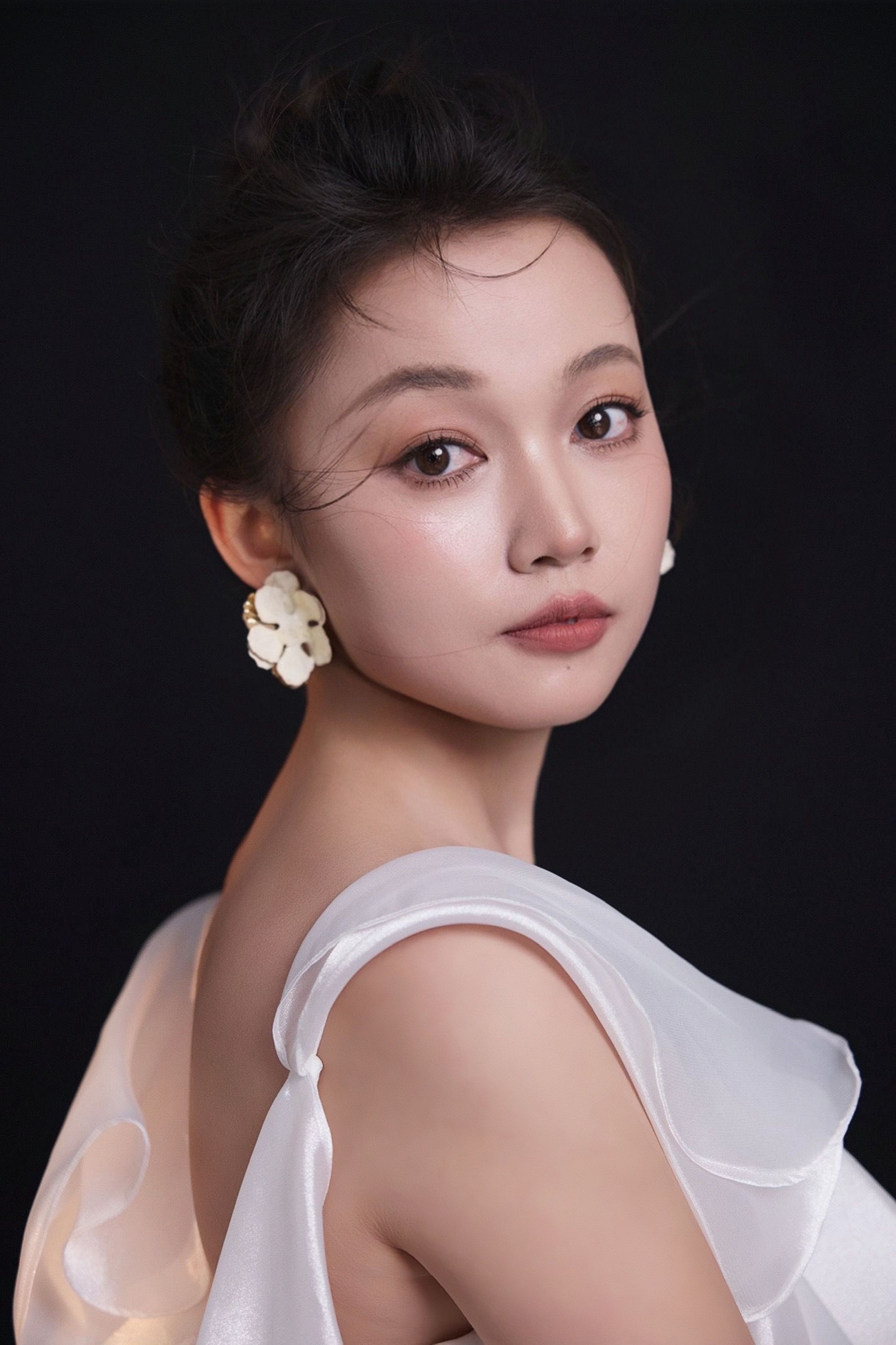 Elegant portrait of a woman wearing a white dress and floral earrings against a dark background.