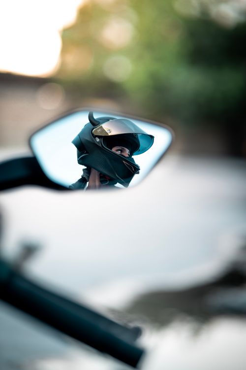 Free A motorcyclist wearing a helmet seen through a rearview mirror on a blurred road background. Stock Photo