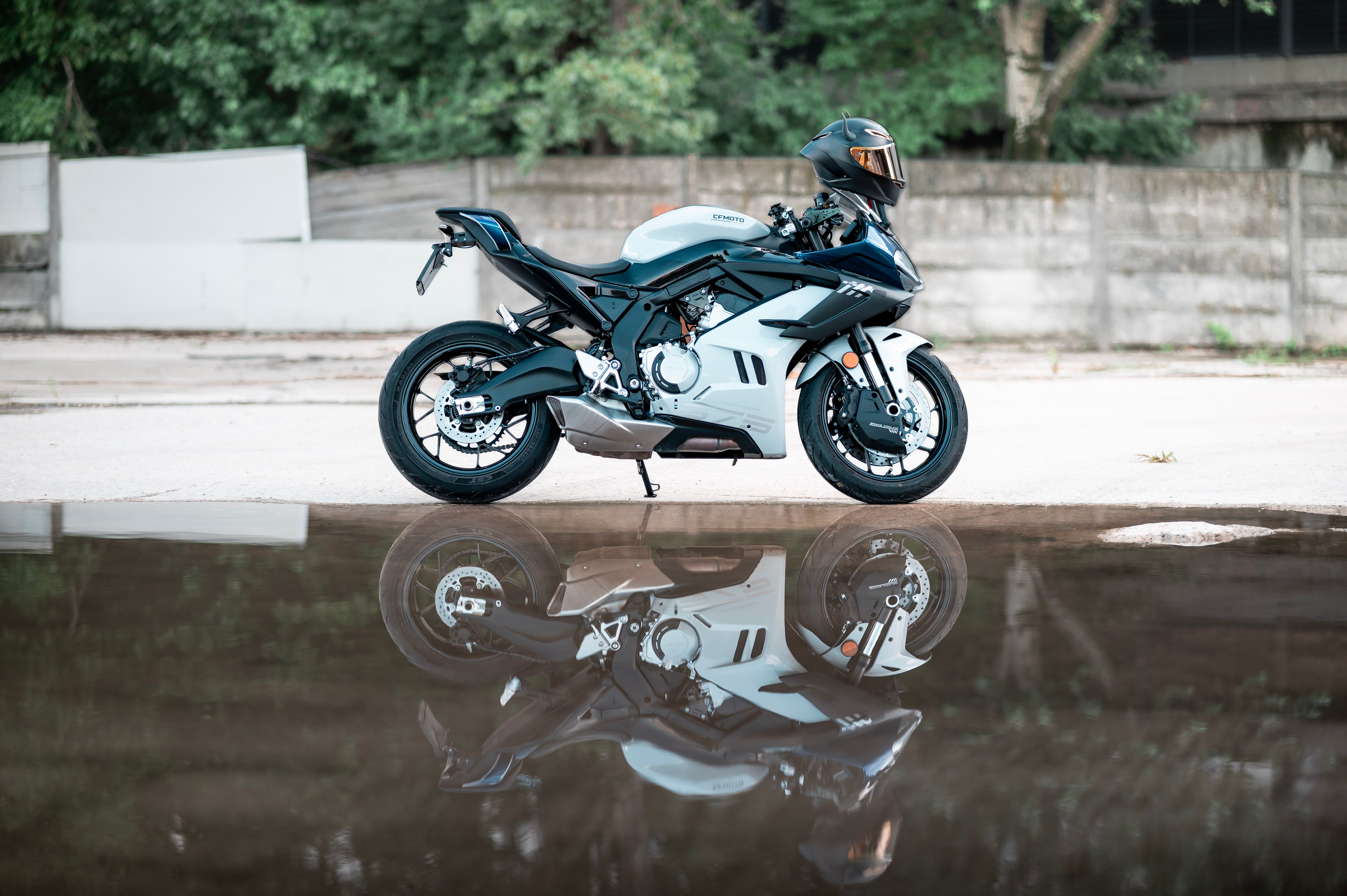 Sport motorcycle reflected in a puddle outdoors with greenery in the background.