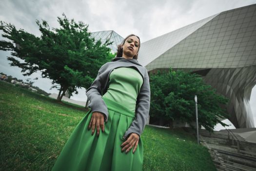 A fashion-forward woman poses confidently in front of a unique architectural building.