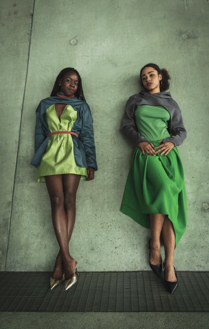 Two stylish women posing in trendy, modern green dresses against a concrete backdrop.