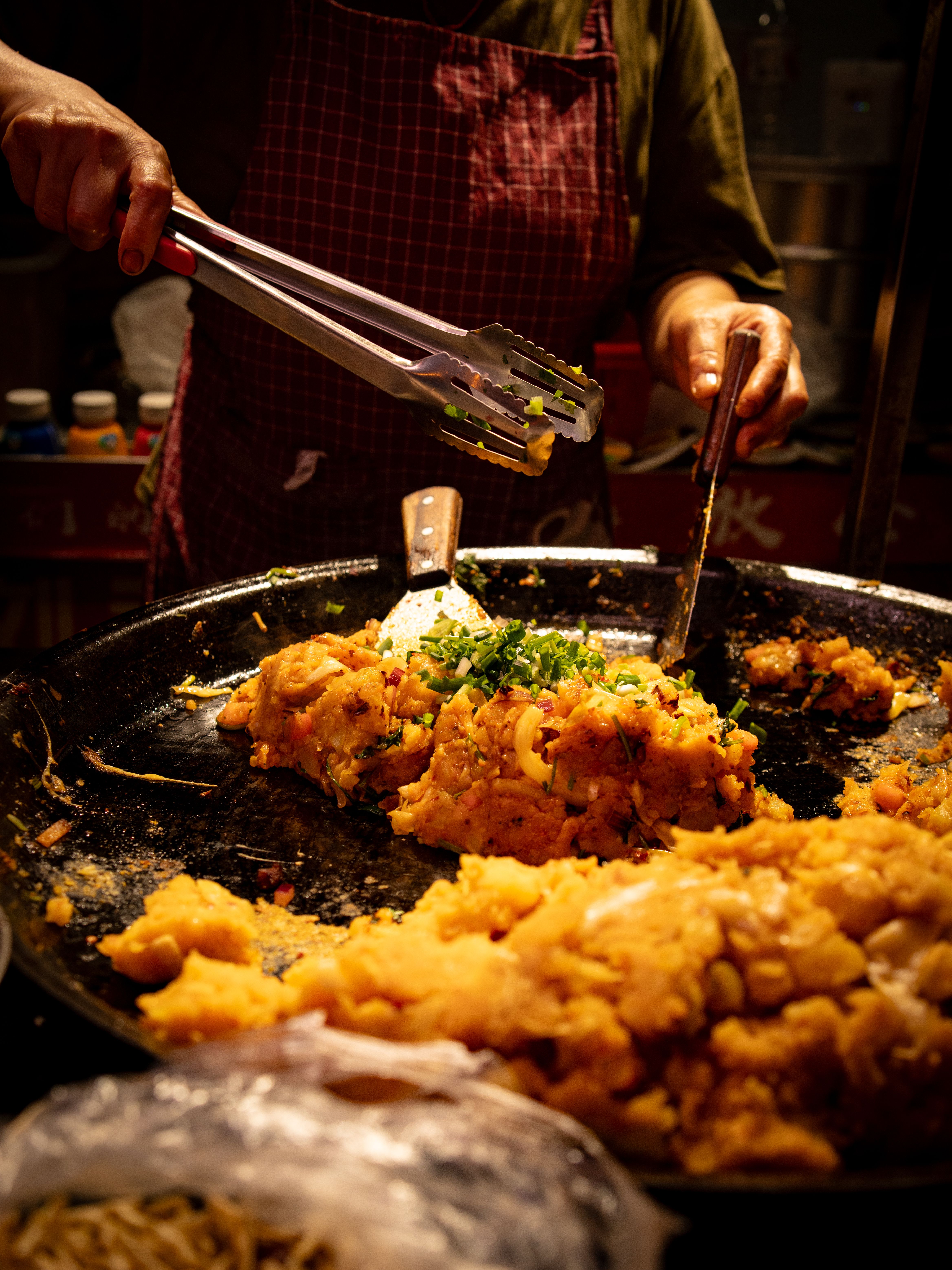 Hands preparing traditional Chinese street food in a wok at a market in Guiyang, China.