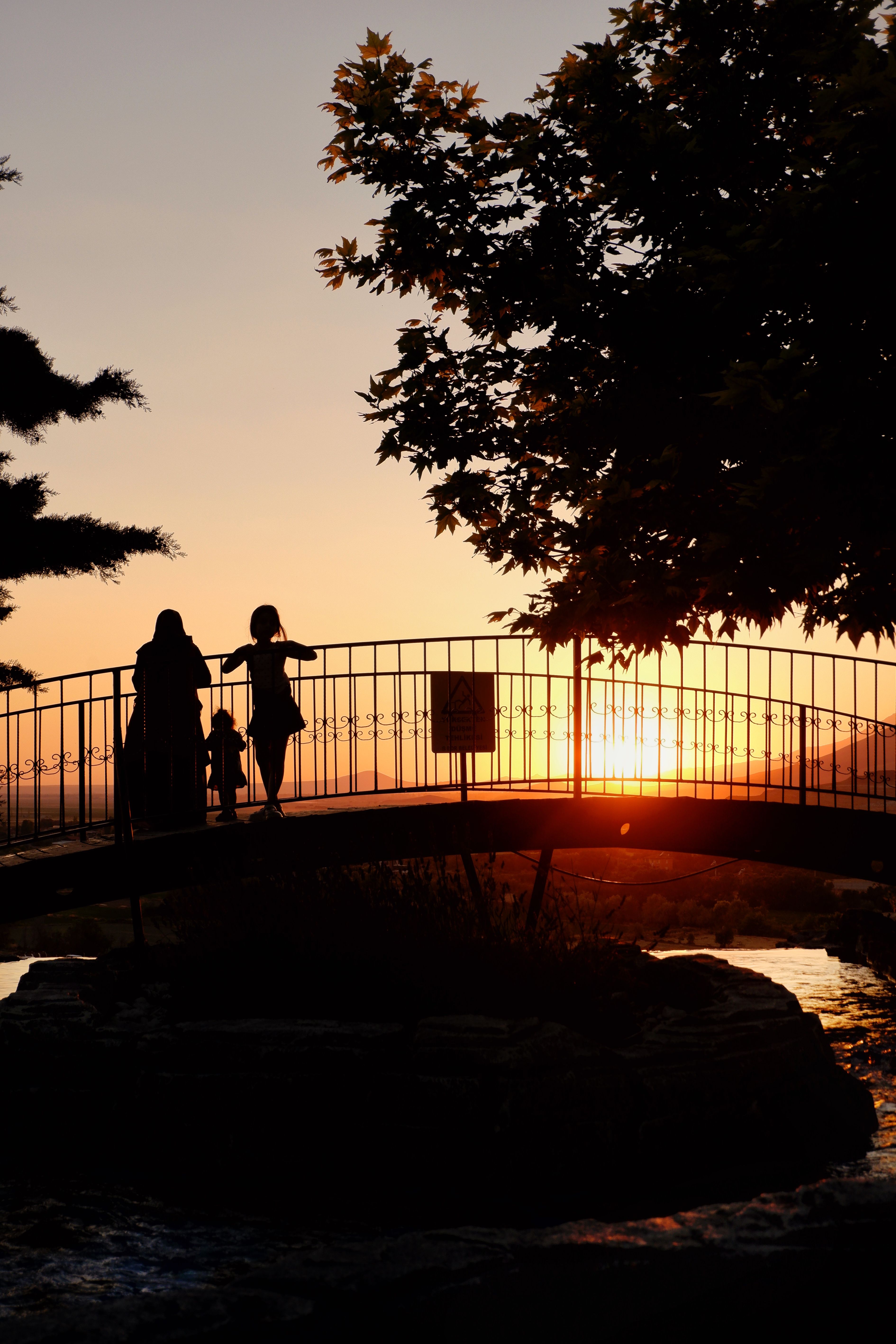 A family silhouette walking on a bridge during a stunning sunset, creating a peaceful scene.
