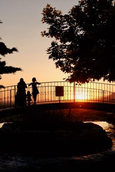 A family silhouette walking on a bridge during a stunning sunset, creating a peaceful scene.