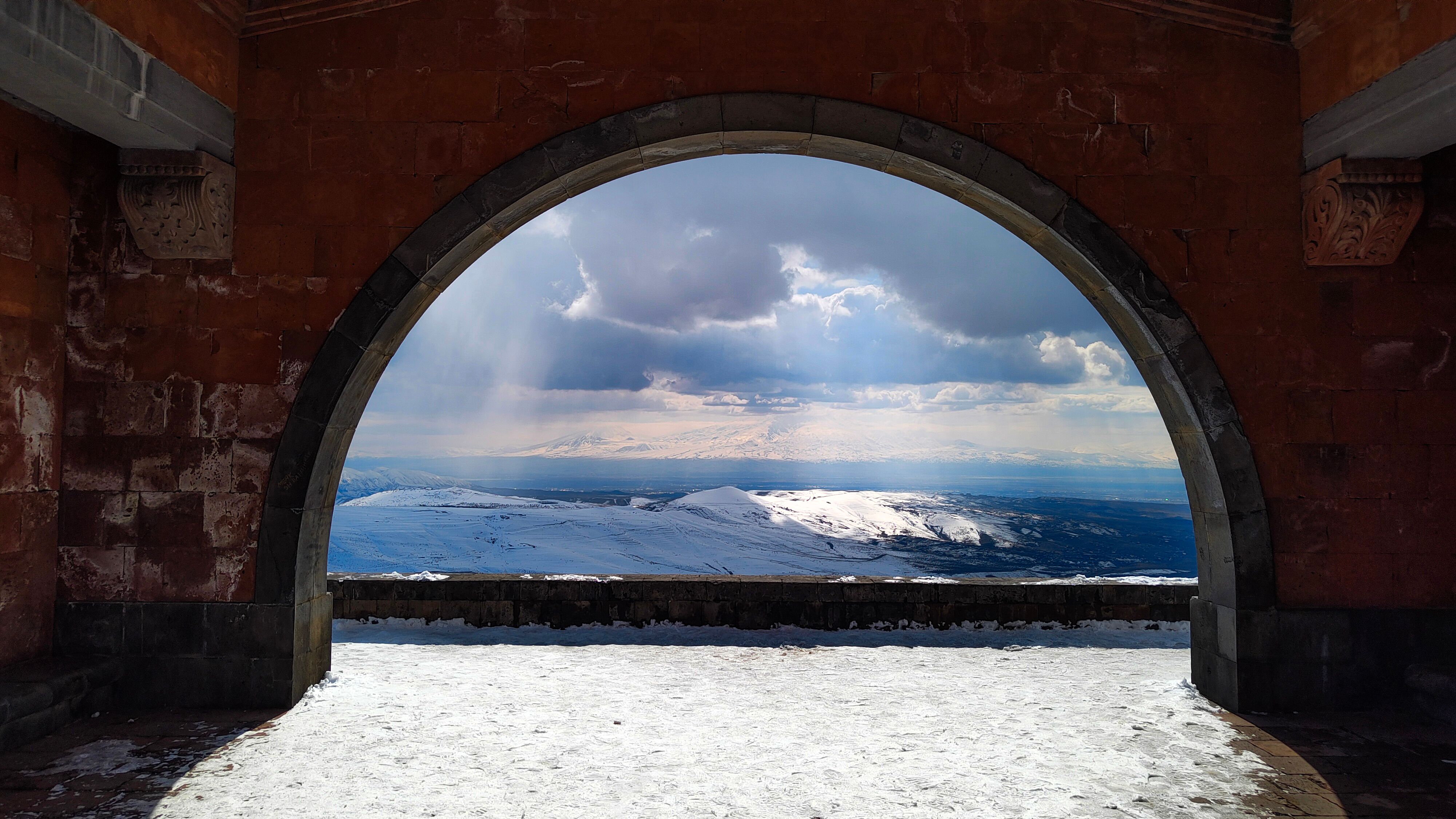 Snow-covered mountains seen through a historic archway in Yerevan, Armenia.