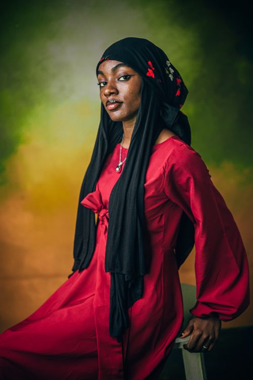 Free Elegant portrait of a woman wearing a red dress and black hijab with floral detail. Stock Photo