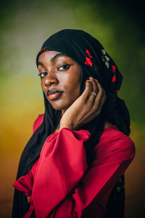 Free Stunning portrait of a woman wearing a red hijab with floral details, set against a vibrant blurred background. Stock Photo