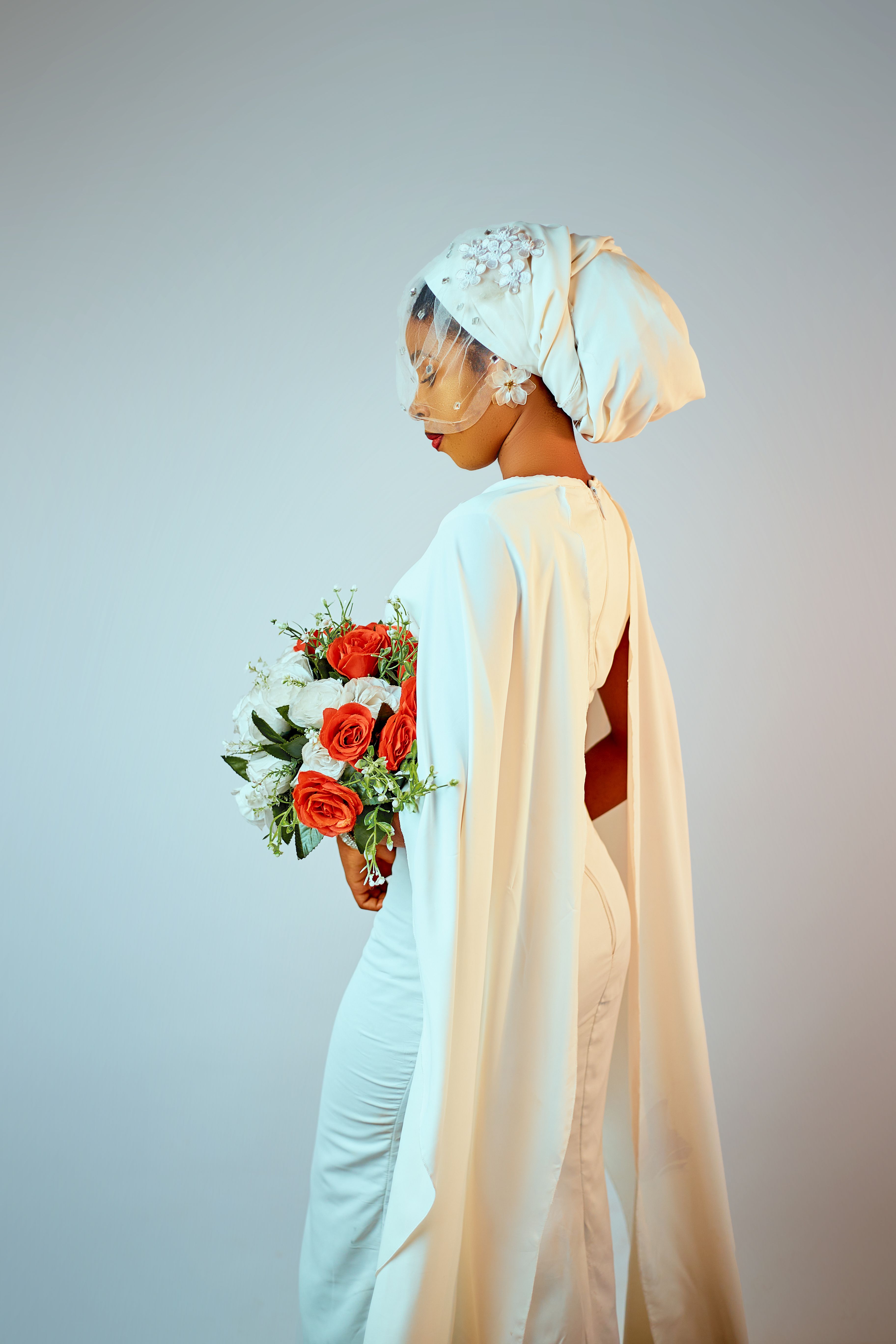 A bride wearing a traditional white outfit and headpiece, holding a bouquet of red and white flowers.