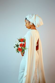 A bride wearing a traditional white outfit and headpiece, holding a bouquet of red and white flowers.