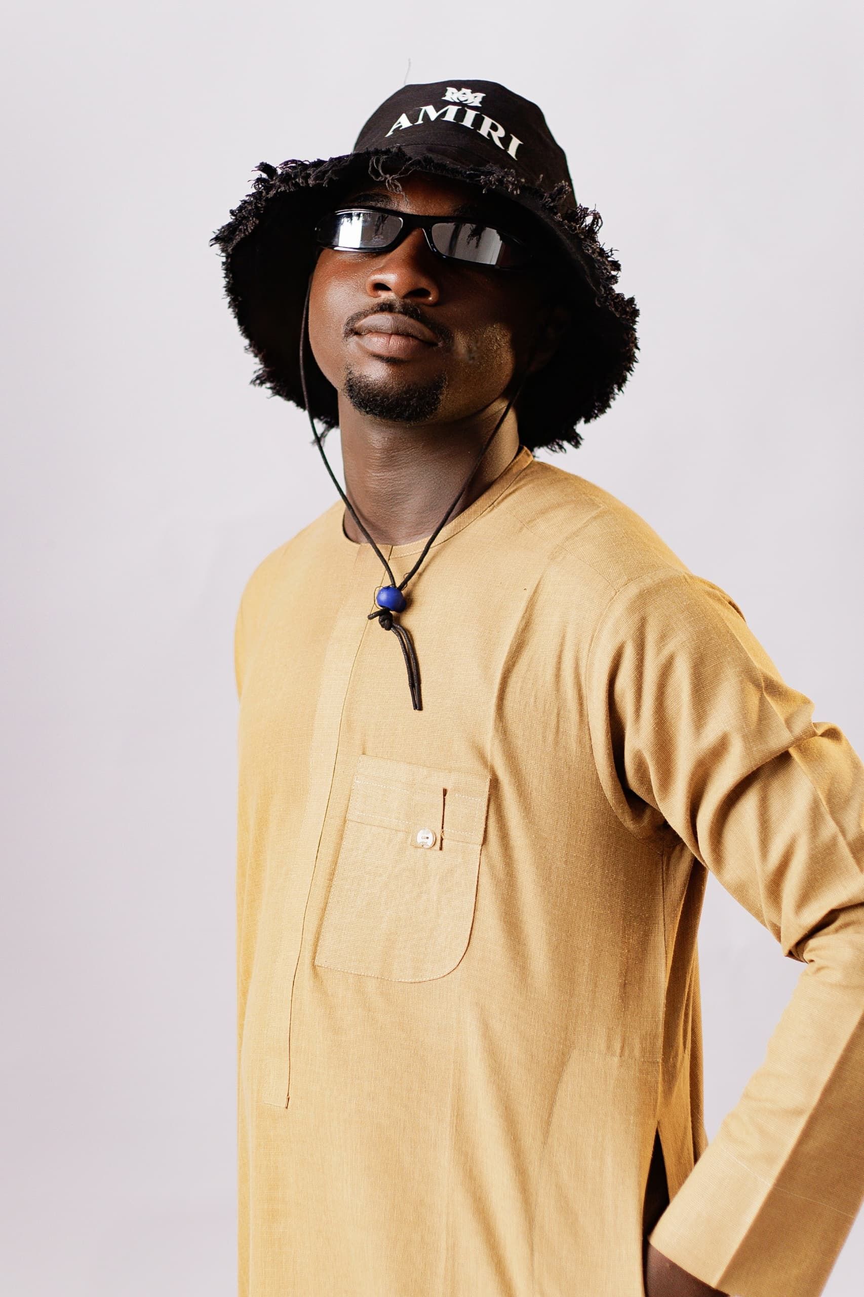 Stylish man wearing a beige kurta and black bucket hat posing confidently.