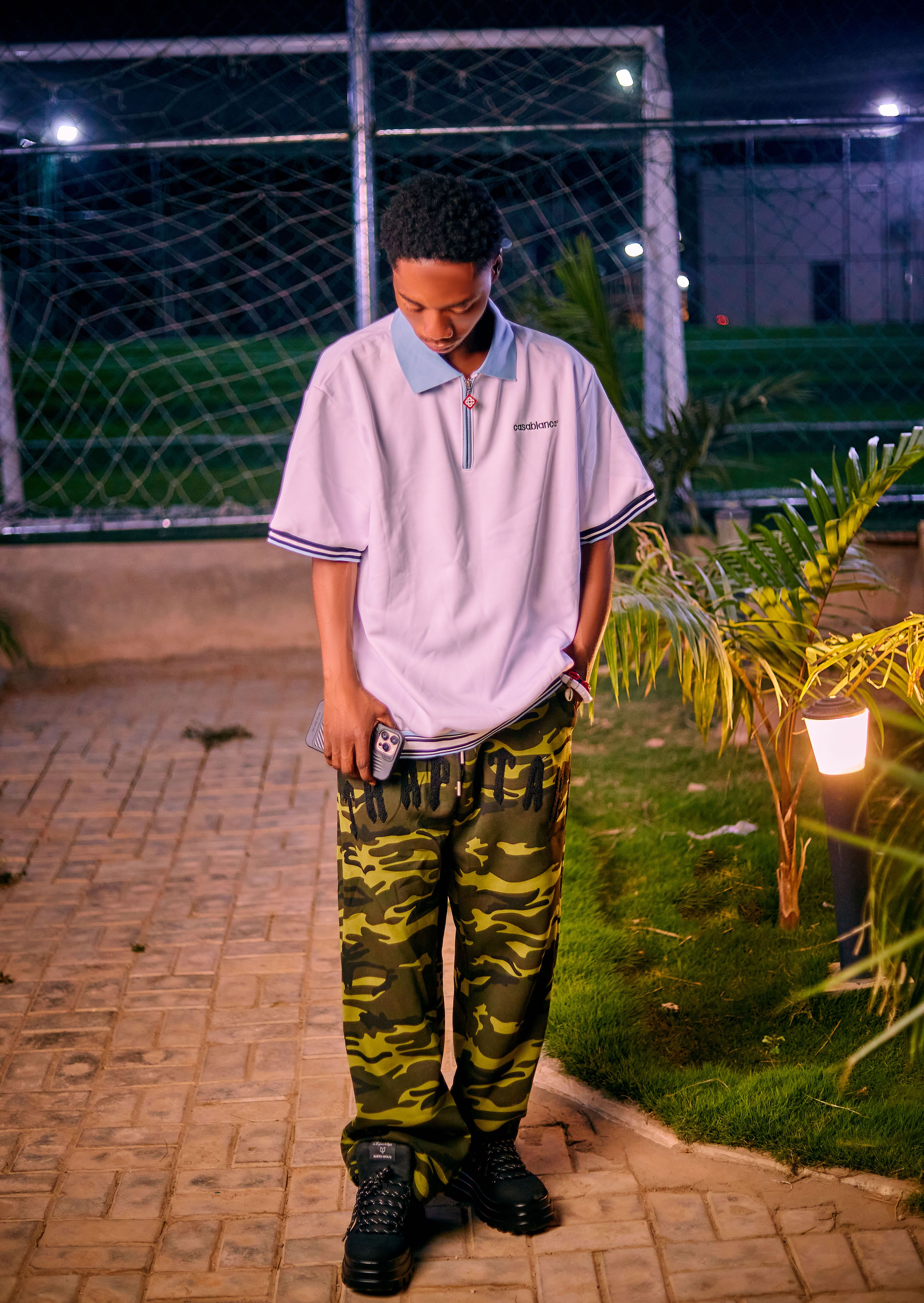 Stylish young person outdoors at night wearing camo pants and a casual shirt.