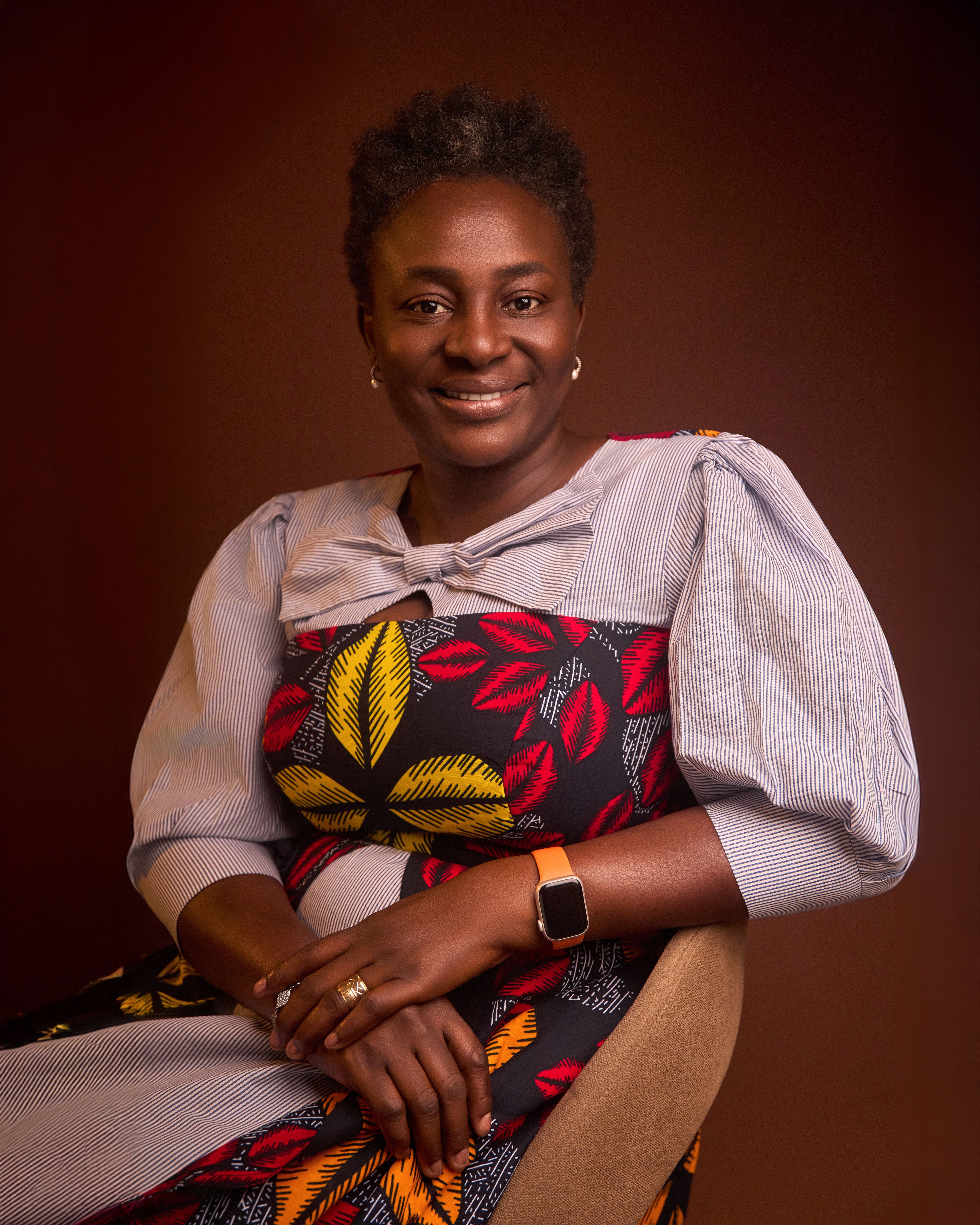 Sophisticated portrait of a woman in a vibrant African print dress, smiling gently.