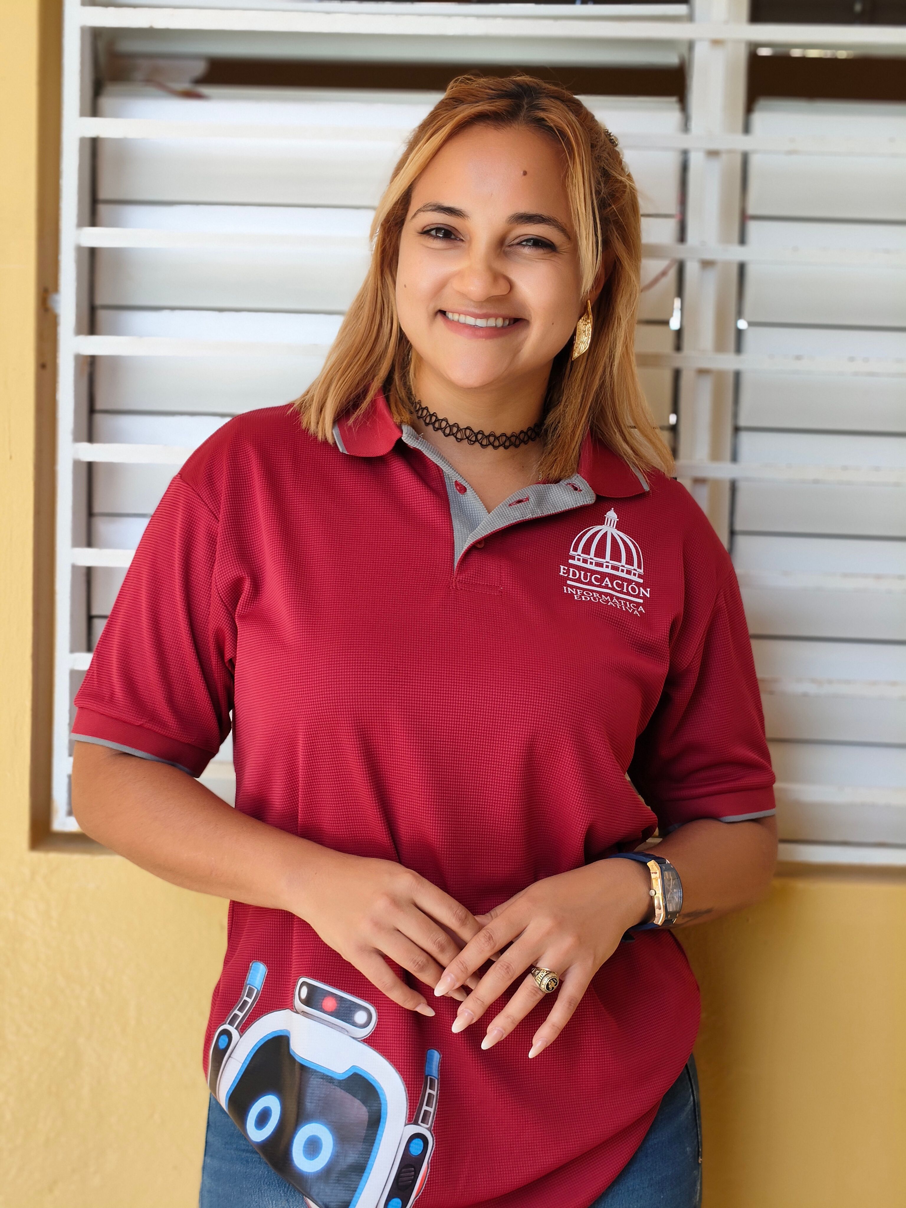 Smiling woman in a red polo inside a classroom, standing confidently.